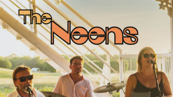 The Neens live band performs on stage with two men on percussion and guitar and a singer with a microphone and sunglasses, outdoors at sunset.