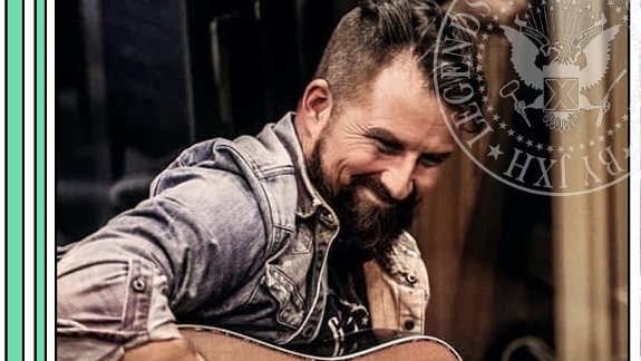 Man playing an acoustic guitar, smiling warmly, wearing a denim shirt; badge overlay reads &ldquo;Leigh Gilbert&rdquo; and &ldquo;Malpractice&rdquo; with guitar+vocals.