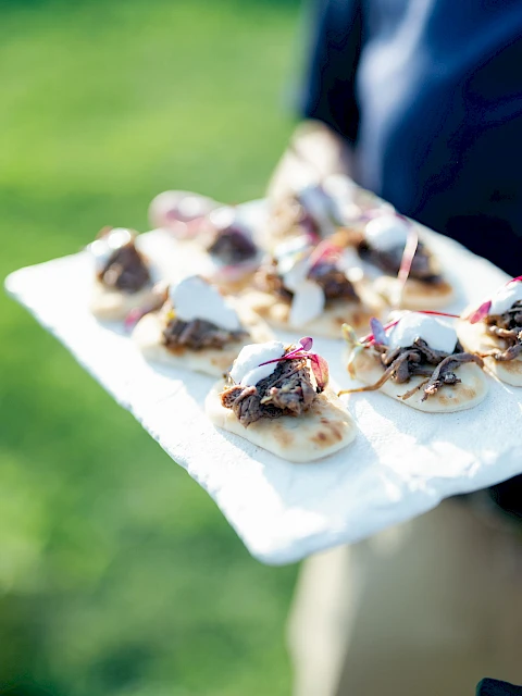 Someone carrying a tray of bite-sized desserts on a paper towel outdoors, with blurred green grass in the background.