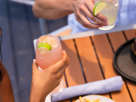 Two people clink glasses of lime-citrus drinks at an outdoor table with fries on the plate.