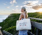 Woman in striped dress on a seaside overlook at sunset, holding a tote bag labeled “Champlin’s Marina & Resort”.