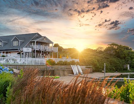 A lakeside resort with a white boardwalk and marina paddleboats at sunrise, glowing under dramatic clouds.