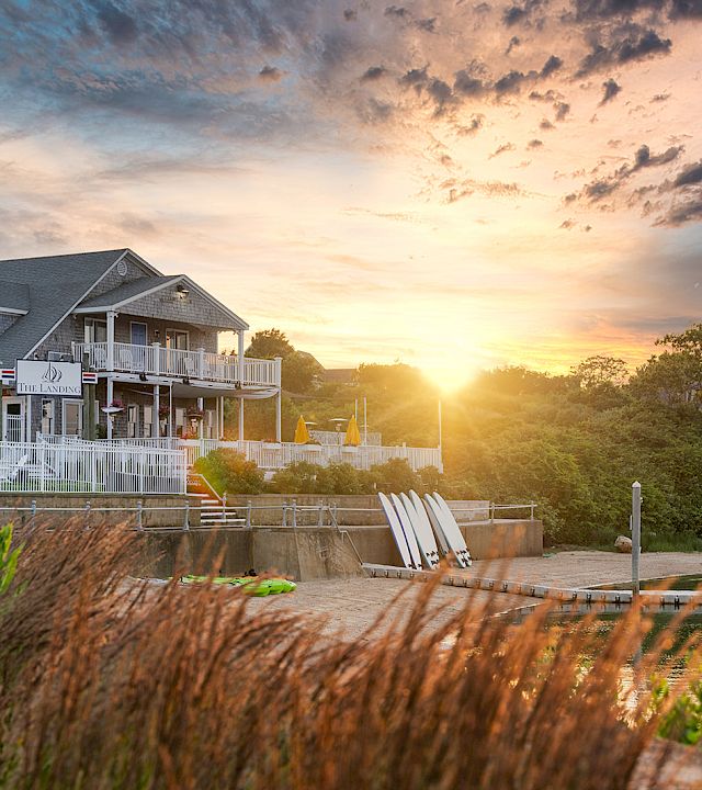 A lakeside resort with a white boardwalk and marina paddleboats at sunrise, glowing under dramatic clouds.