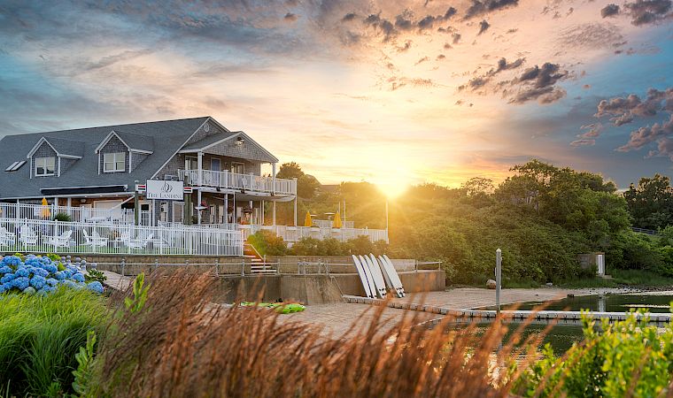 A lakeside resort with a white boardwalk and marina paddleboats at sunrise, glowing under dramatic clouds.