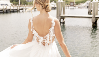 A person in a white dress stands by a marina, with boats and green hills in the background.